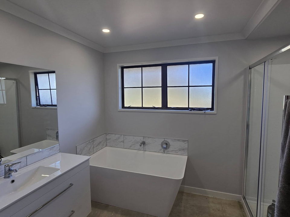 After: a freestanding bath under a new window, white walls and a glass shower beside it