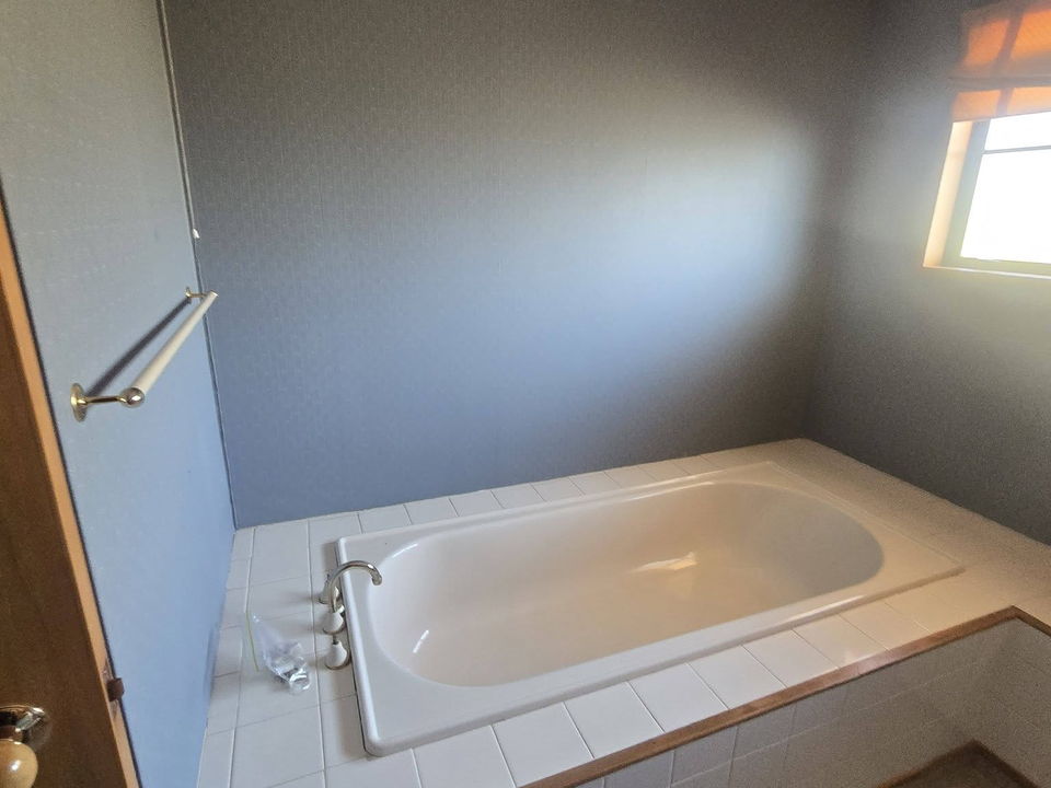Before: an older bath set in a tiled surround, with wallpapered walls and a small window