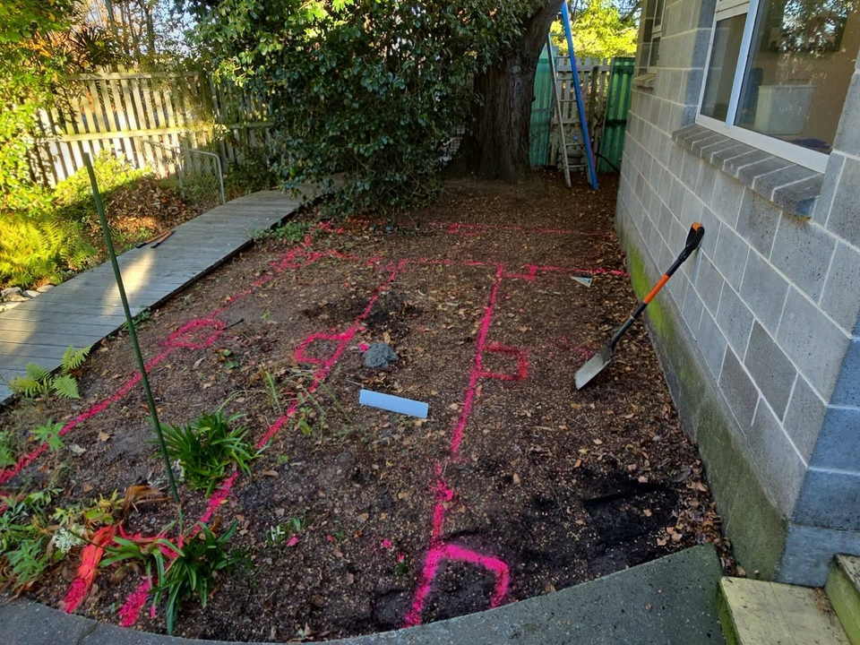 Before: a garden bed beside the house cleared and marked out with pink spray paint for the new deck
