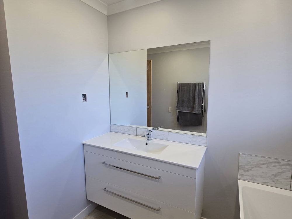 White floating vanity under a wide mirror, the bathroom part way through finishing