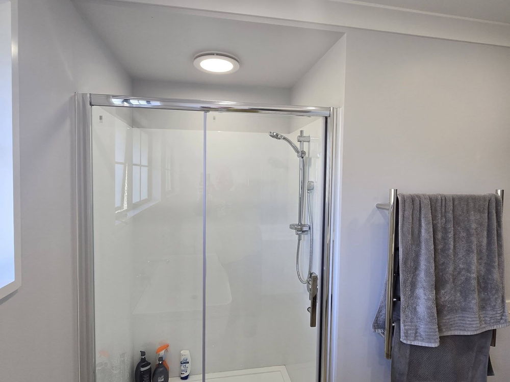 Large glass shower with a chrome frame in a white bathroom, towels on the rail