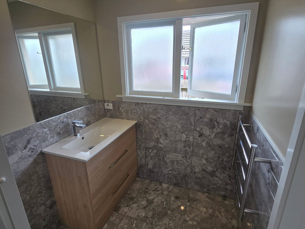 Wall-hung timber-look vanity and a heated towel rail against grey tiles