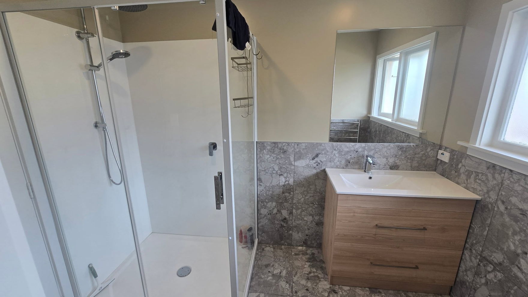 Renovated bathroom with a glass shower, a timber-look wall-hung vanity and grey stone-look tiles on the floor and walls