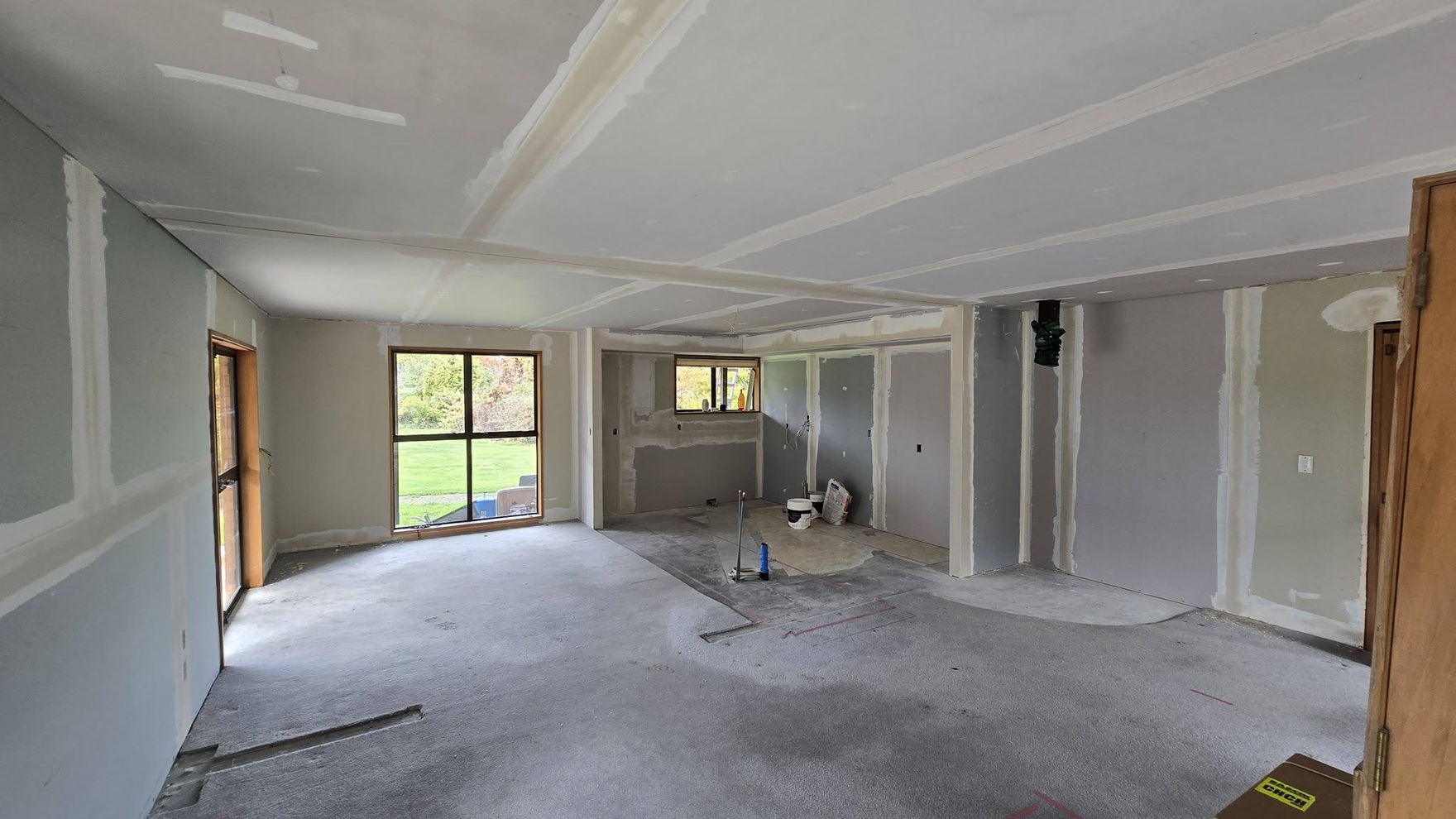 Newly lined open-plan room with the plasterboard joints stopped, looking towards the windows and a doorway