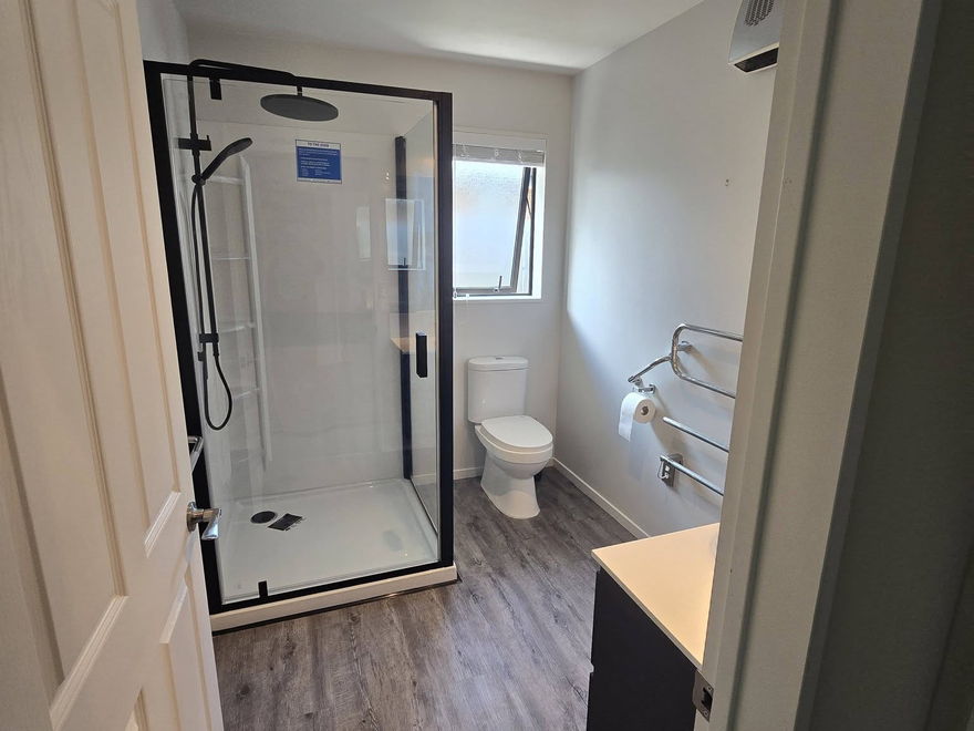 Black-framed glass shower on a raised base in a renovated bathroom, with a heated towel rail and a new vanity