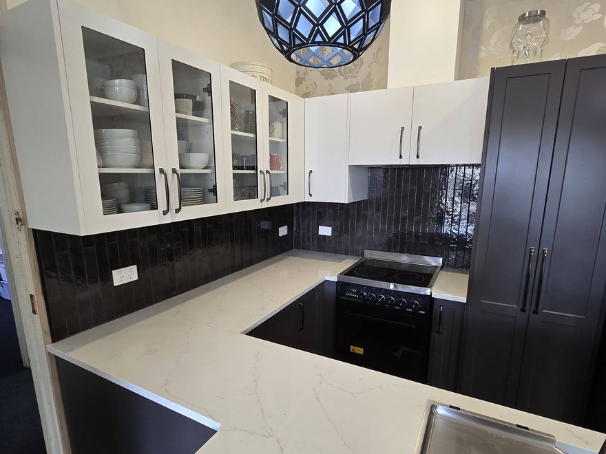 Renovated kitchen with a white stone benchtop, dark cabinetry, a black tiled splashback and a patterned pendant light